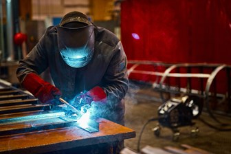 A welder working with raw material to create hydraulic hose components.